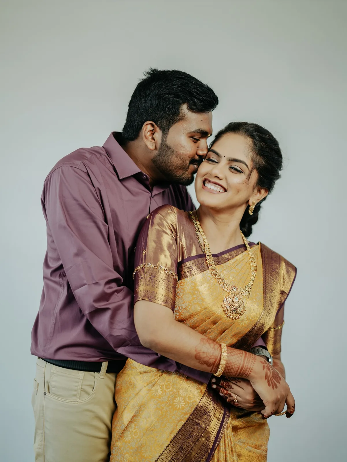 A couple laughing as he kisses her cheek on their engagement day