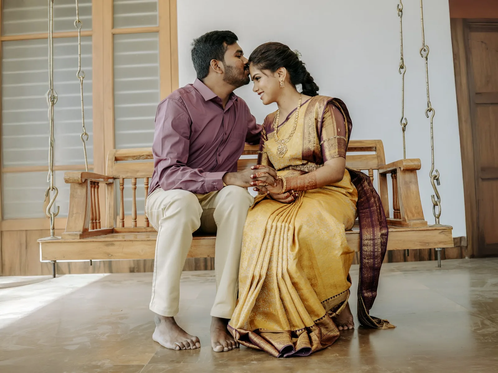 The couple seated on a wooden swing, his forehead kiss
